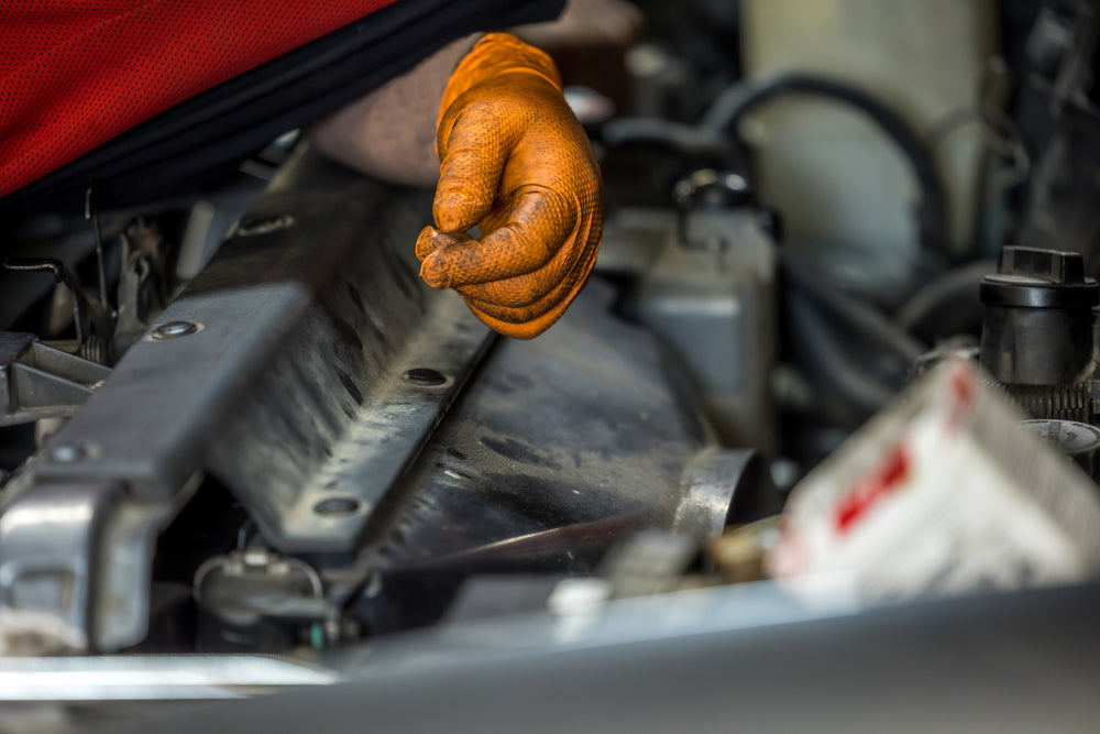 Mechanic's hand wearing Outrageous Orange Nitrile Gloves working on a cars engine.